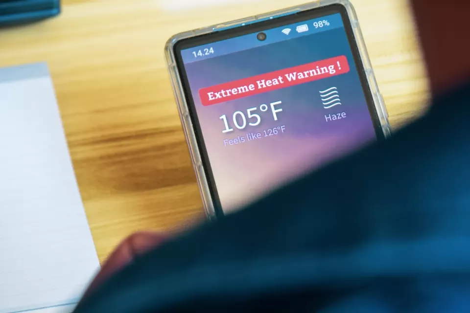 Close-up over shoulder of person holding smartphone with extreme heat warning and 105 degree temperature indicated.